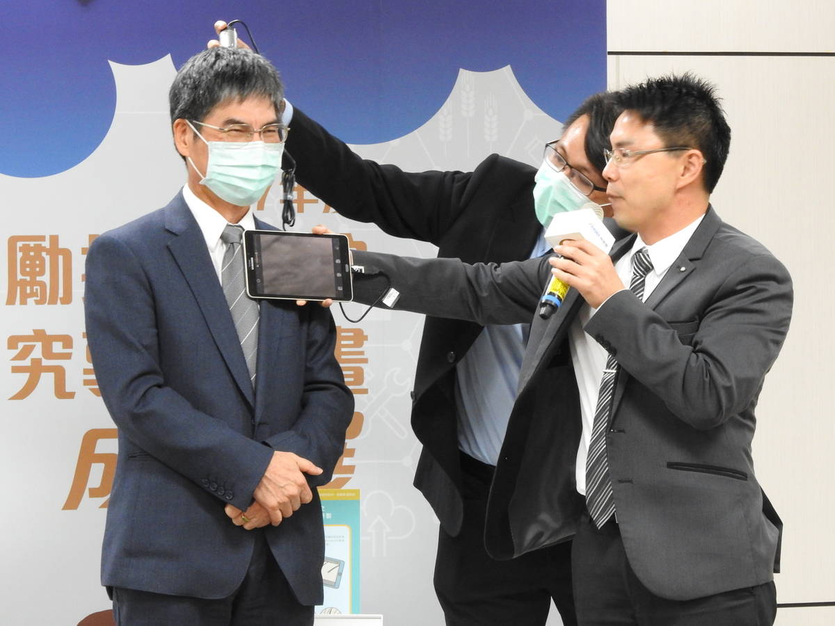 南臺科技大學電子工程系副教授張萬榮以「智能頭皮膚質檢測系統」為科技部部長檢測頭皮健康。(科技部提供)