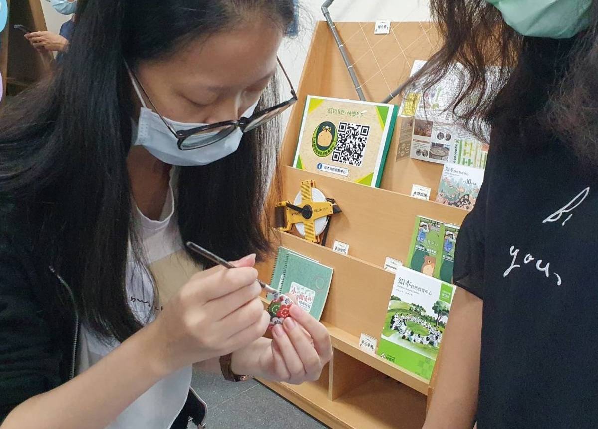 臺東縣自然史教育館攤位中指導學生利用回收的蛤蜊殼，結合花色繽紛的千代紙，手作獨一無二的精美小吊飾。