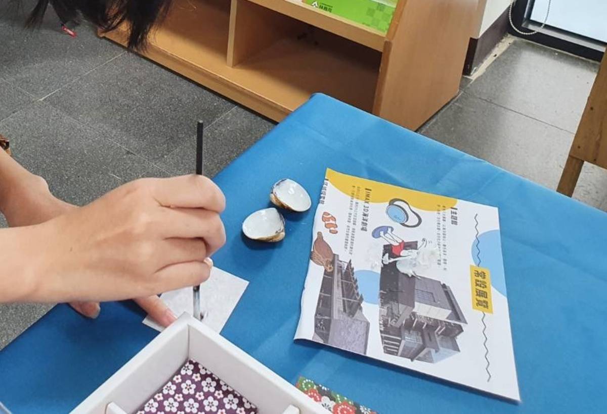 臺東縣自然史教育館攤位中指導學生利用回收的蛤蜊殼，結合花色繽紛的千代紙，手作獨一無二的精美小吊飾。