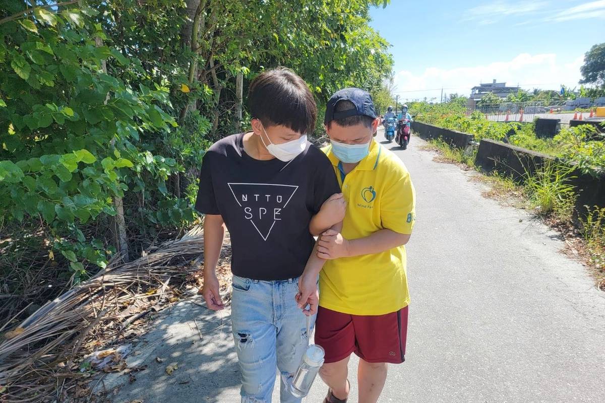 緊緊挽著志工的手臂，患有多重障礙的牧心學員，在臺東大學特教系學生李宇翔的攙扶下緩步前進。