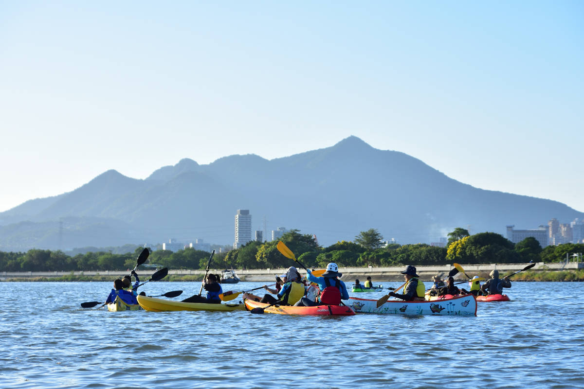 學生在基隆河上划著獨木舟，欣賞觀音山美麗山景