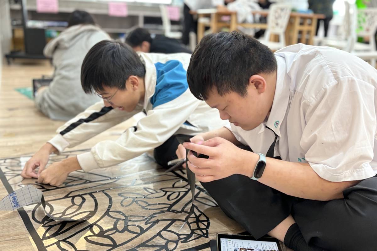 學生坐在地板上專心製作，將黑色線條貼在透明片上。