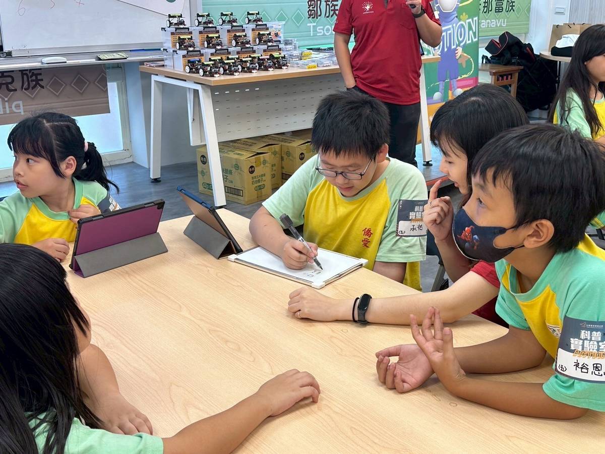 僑愛國小學生圍在一起比對程式碼，專心討論如何修正小車的運行路線