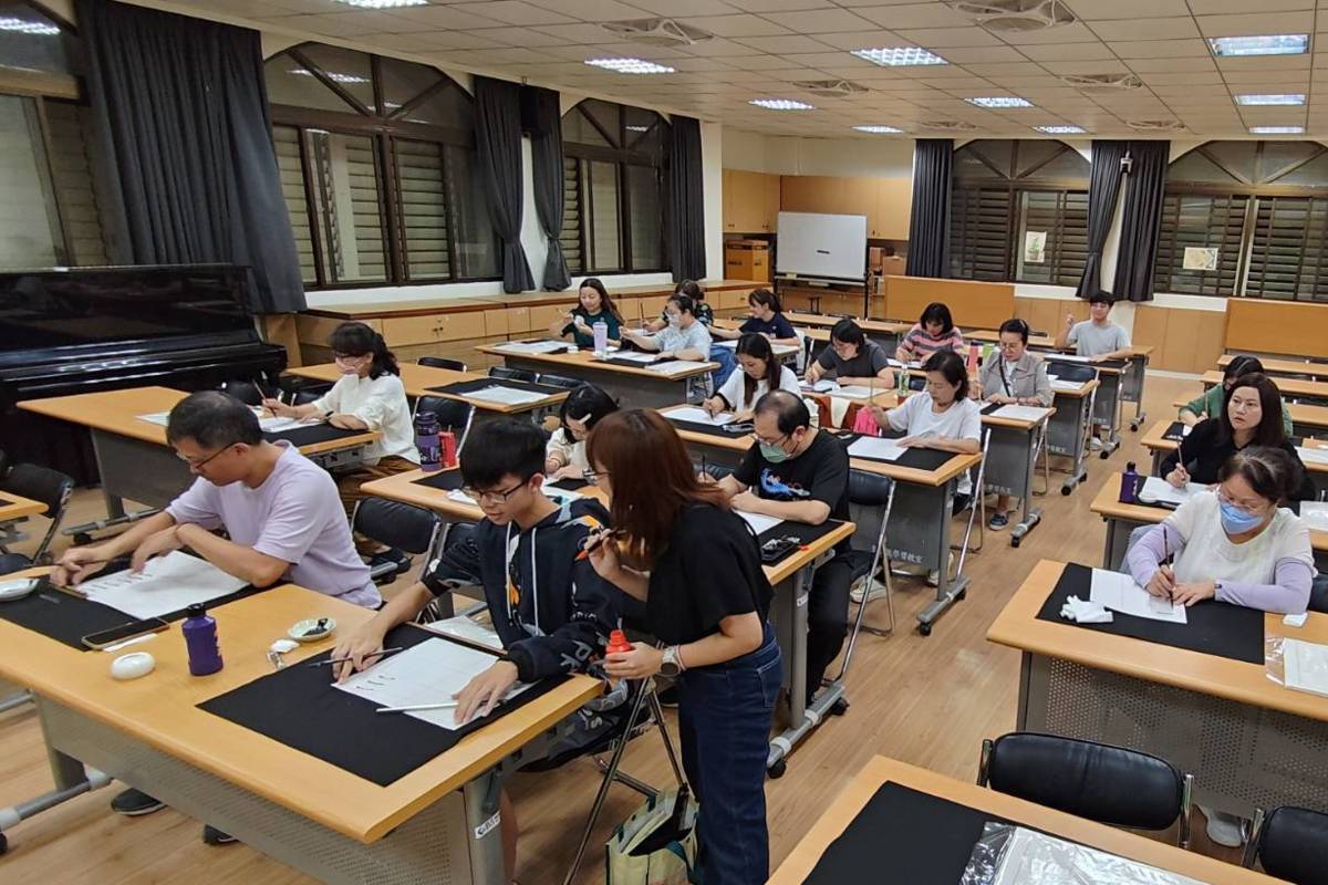 一群對熱愛書法的社區民眾在教室安靜坐好，向老師黃寀霓學習寫書法。